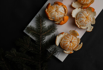 sweet orange juicy tangerines in a peeled peel lie on a black background and a white marble board with a spruce Christmas branch.for cards, banners, flyers, invitations