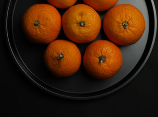 sweet orange round juicy whole tangerines lie on a black background round black tray.for postcards banners flyers invitations