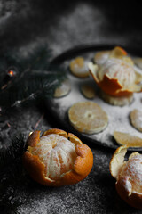 sweet orange juicy tangerines in a peeled peel lie on a black background and a black kitchen tray next to a spruce Christmas branch and sprinkled with white powder.for cards, banners, flyers, invitati