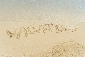 Word Vacation on beach - summer concept background. Sea, wave,  inscription vacation on the sand. The wave washes away the inscription vacation on the sand. Vacation ending concept.