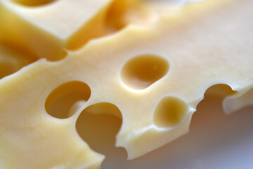 Pieces of yellow cheese with large holes on a white background. Delicious cheese close-up.