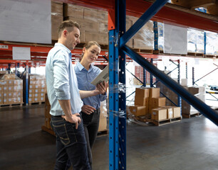Fototapeta na wymiar Distribution warehouse manager and client businesswoman using digital tablet checking inventory storage on shelf. Storehouse supervisor worker and logistic engineer standing together at storage room.