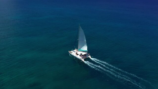 Aerial footage, rear view of luxury sailboat sailing on a deep blue sea with white wakes. Camera follow catamaran in blue ocean water