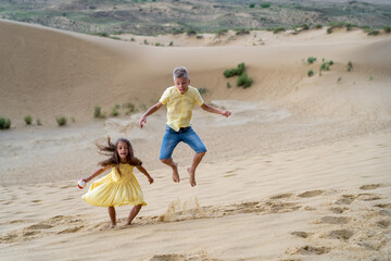 Children jump on sand dunes through sand dust driven by wind on summer holidays