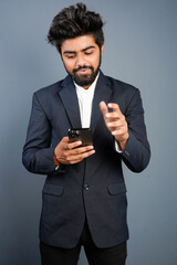 Portrait of a handsome happy young businessman wearing suit standing isolated over gray background, using mobile phone, video call concept