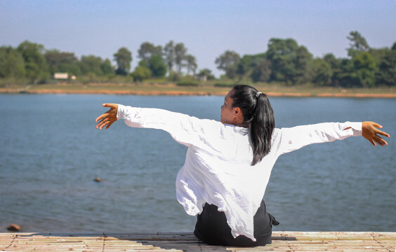 Asian woman sitting with arms outstretched by the water relaxing