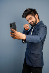 Portrait of a handsome happy young businessman wearing suit standing isolated over gray background, using mobile phone, video call concept