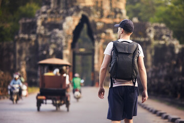 Man with backpack is walking to ancient city. Rear view of tourist, Siem Reap, Cambodia..
