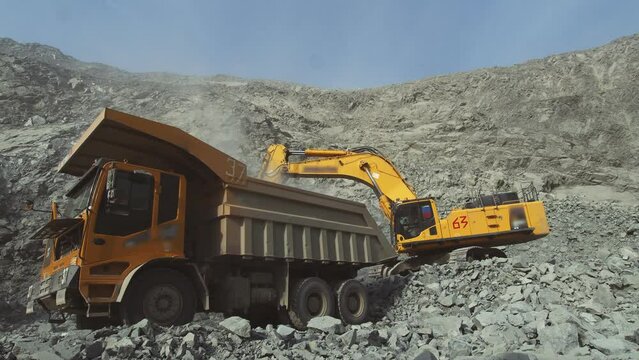 Cargo dump truck being loaded in a mining quarry. Yellow excavator loads mineral resource into the back. Quarry for the extraction of valuable minerals.
