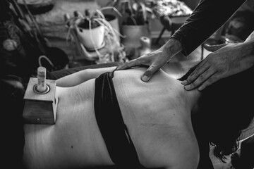 Obraz premium Traditional chinese medicine doctor in the consult doing a massage to a teenager girl patient with herbal moxa stick in a smoke box in the back (moxibustion) (in black and white)