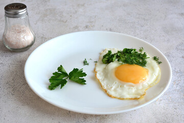 fried egg with yolk on white plate with parsley isolated, close-up