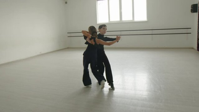 Boy and girl waltzing in a dancing hall near the mirror. Pair wear black clothing. Dancing lesson in a dancing hall flooded with sunlight. High quality 4k footage