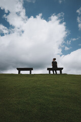 Rear view point ofyoung woman relaxing on a park bench ,with green grass ,blue sky and cloud