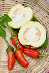closeup the bunch ripe yellow white guava fruit sliced with red chilly and green leaf in the brown basket soft focus natural white brown background.
