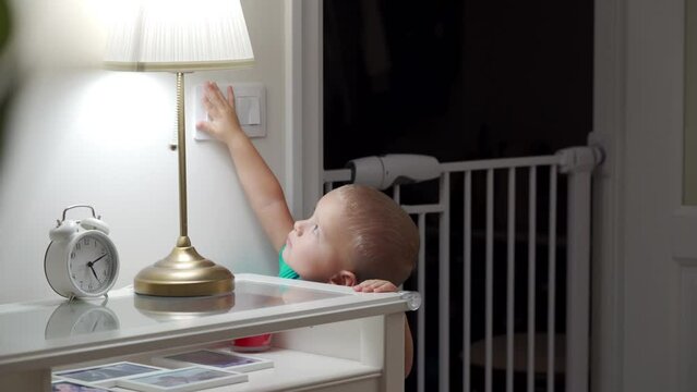 Little toddler child is playing with light switch, turning on off the light in the room.