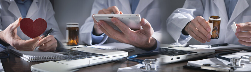 Caucasian doctor holding bottle of pills, red heart and using tablet computer.