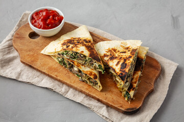 Homemade Spinach and Mushroom Quesadilla with Salsa on a rustic wooden board