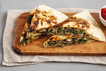 Homemade Spinach and Mushroom Quesadilla with Salsa on a rustic wooden board, low angle view