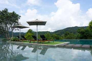 Deck pool chairs beside the swimming pool with mountain background in Chiang Mai, Thailand