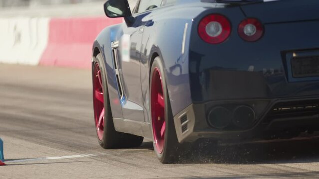 Back view of a modern shiny sport car abruptly starts from the spot, slips, during race on the track. Smoke billows from the exhaust pipe, it's a sunny day