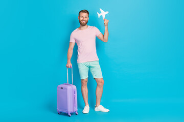Full length photo of nice young man travel suitcase hold paper plane free air miles wear trendy pink look isolated on cyan color background