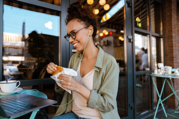 Hispanic woman working with laptop while having breakfast at cafe