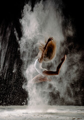 Dancing girl in a jump with dust flour powder on black background. Gymnastics 