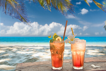 two cocktails on the tropical beach with blue sky and palm leafs in the background