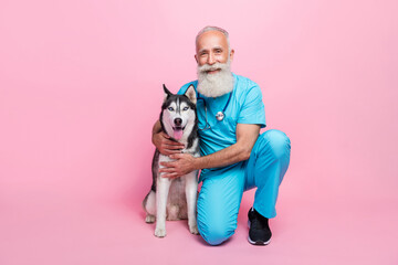 Full length photo of nice professional old doc dressed blue uniform stethoscope on neck cuddle husky isolated on pink color background