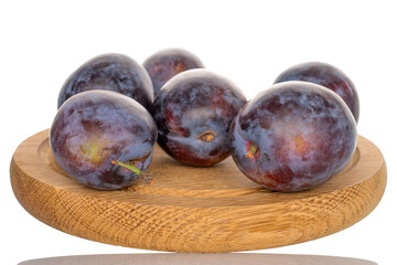 Several organic plums on a round wooden tray, close-up, isolated on a white background.