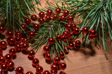 Shiny red beads on a wooden surface with a pine branch, the celebration of the new year holiday