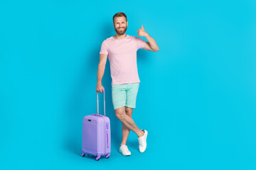 Full length photo of nice young guy baggage thumb up business trip dressed stylish pink outfit isolated on aquamarine color background