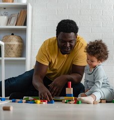 Father supporting their cute little daughter in playing with colorful didactic wooden toys at home