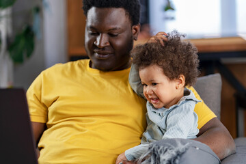 Obraz premium Father spends time with a cute daughter watching a laptop computer with her. Multicultural family. Educational apps for small kids.