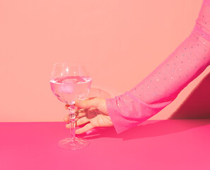 Pink gin cocktail in a highball glass and female hand against bright wall. Girls party idea. 