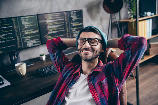 Photo of positive smiling guy dressed eyewear arms hands behind head closed eyes indoors workstation workshop home