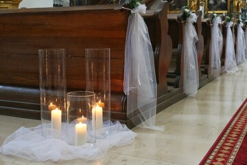 Candles and bouquets with white sashes constituting the wedding decoration of the church.