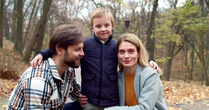 Close-up portrait of charming young blonde woman beautiful handsome man and cute happy little son looking at camera smiling. Lovely family of dad mom and boy standing in autumn park hugging.