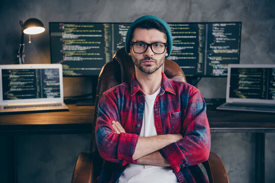 Photo of serious confident programmer wear spectacles arms folded sitting indoors workplace workshop home
