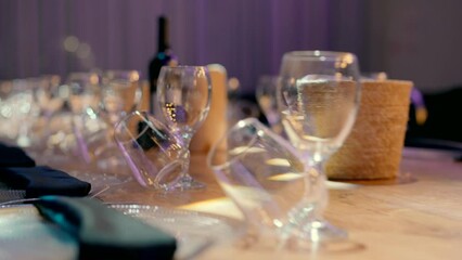 A beautiful wooden dining table for a wedding for many guests. A bottle of wine, wine glasses, plates with black napkins on them on a wooden table in an event hall