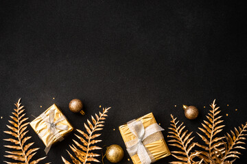 Christmas flat lay background. Palm leaves, present box and golden decorations on black. Top view...