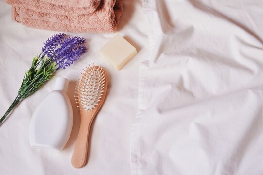 Beige towel, white shampoo bottle, wooden comb, natural soap and lavender flowers. Organic bath products. Flat lay photo, top view. Image for design site and beauty blog