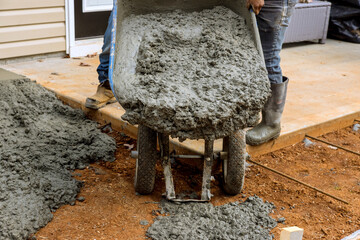 Workers are using wheelbarrow wet cement to sidewalk path near house by pouring wet cement concrete