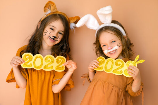 Funny girls show the numbers 2022 and 2023 of the new year. Children dressed up in animals with tiger and rabbit painted on their faces