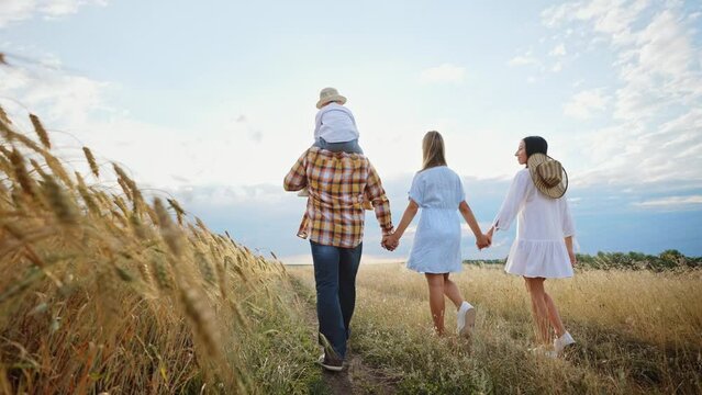 Happy family walks in wheat field holding hands, talking and gesturing. Parents and children walk on outdoors nature landscape. Friendship, love, support, unity. Hiking or travel. Leisure activity.