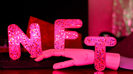 NFT inscription with glitter and artificial hand. Non-Fungible token lettering in pink neon light. Futuristic cryptocurrency concept