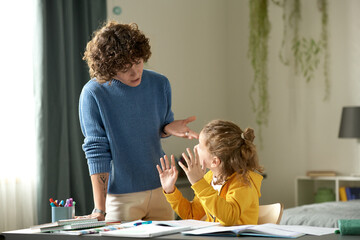 Young mom talking to her child in rude manner, she explaining him chool material while he sitting...