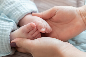 Close-up of a mother's hands cradling the feet of her newborn Caucasian child. The impact of...