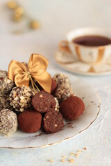 Obraz na płótnie Canvas Chocolate truffles coated in a sprinkling of walnuts and cocoa on a white plate with a gold stripe, decorated with a gold bow on a white background, a warm Christmas atmosphere, xmas decorations.