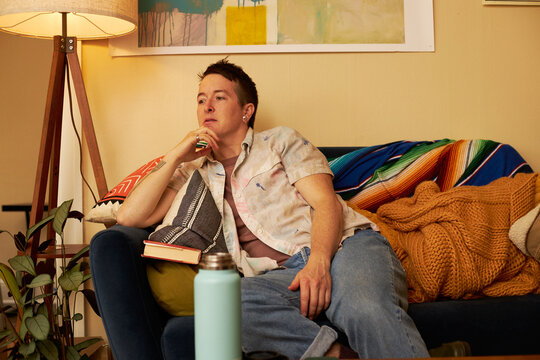non binary person sitting on couch looking away
